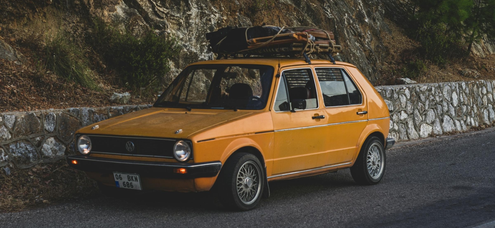 Klasični žuti VW Golf 1 sa krovnim prtljagom na planinskom putu kao simbol putovanja i ekonomičnosti