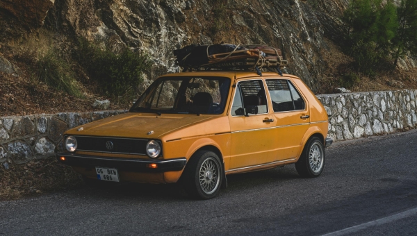 Klasični žuti VW Golf 1 sa krovnim prtljagom na planinskom putu kao simbol putovanja i ekonomičnosti