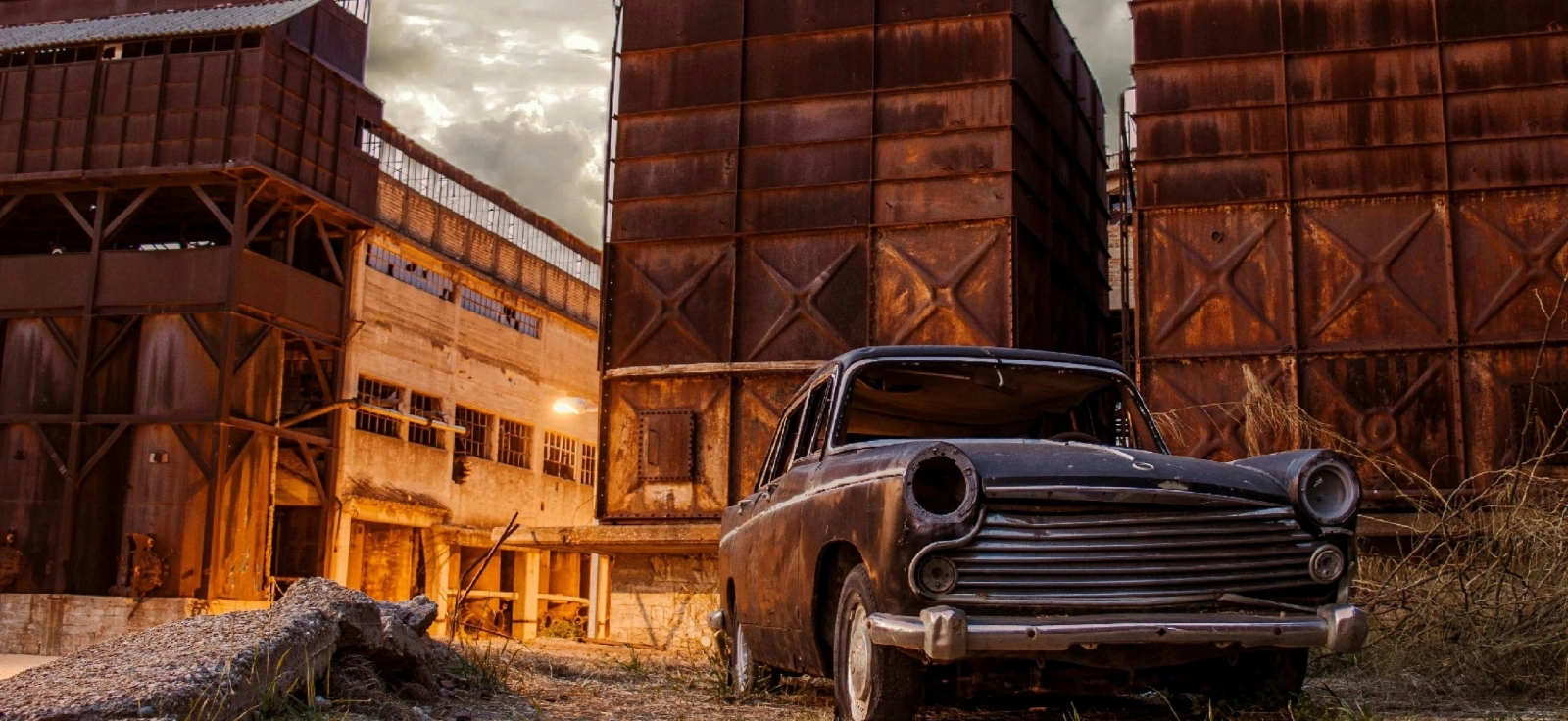 Automobil koji više nije u voznom stanju ispred napuštene auto farbike.