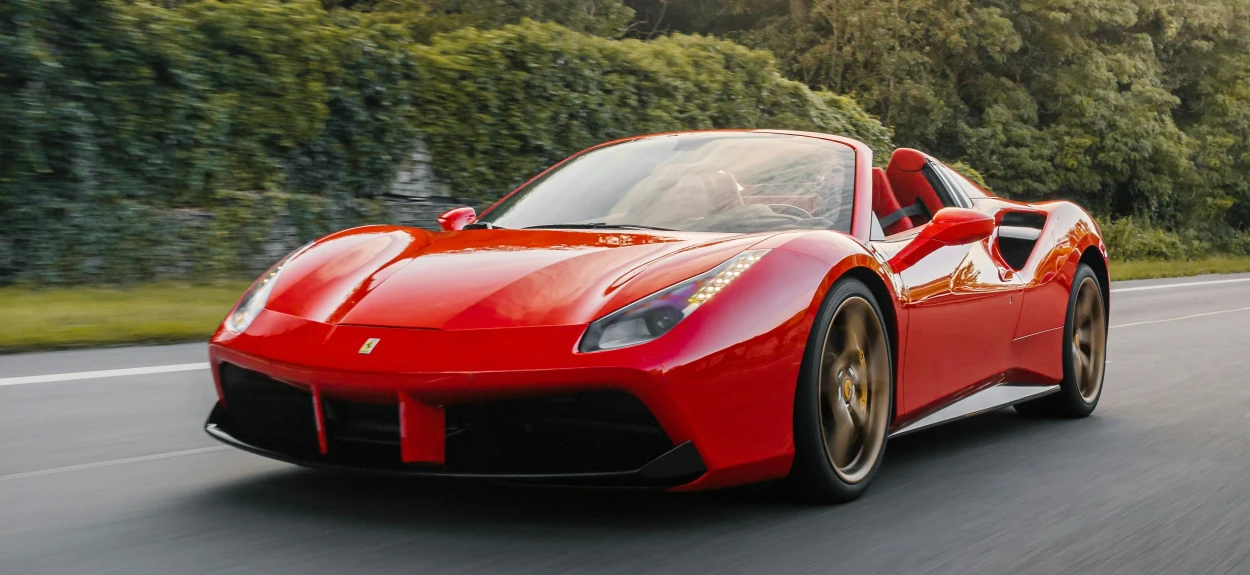 Crveni Ferrari u voznji kako prolazi pored šume.